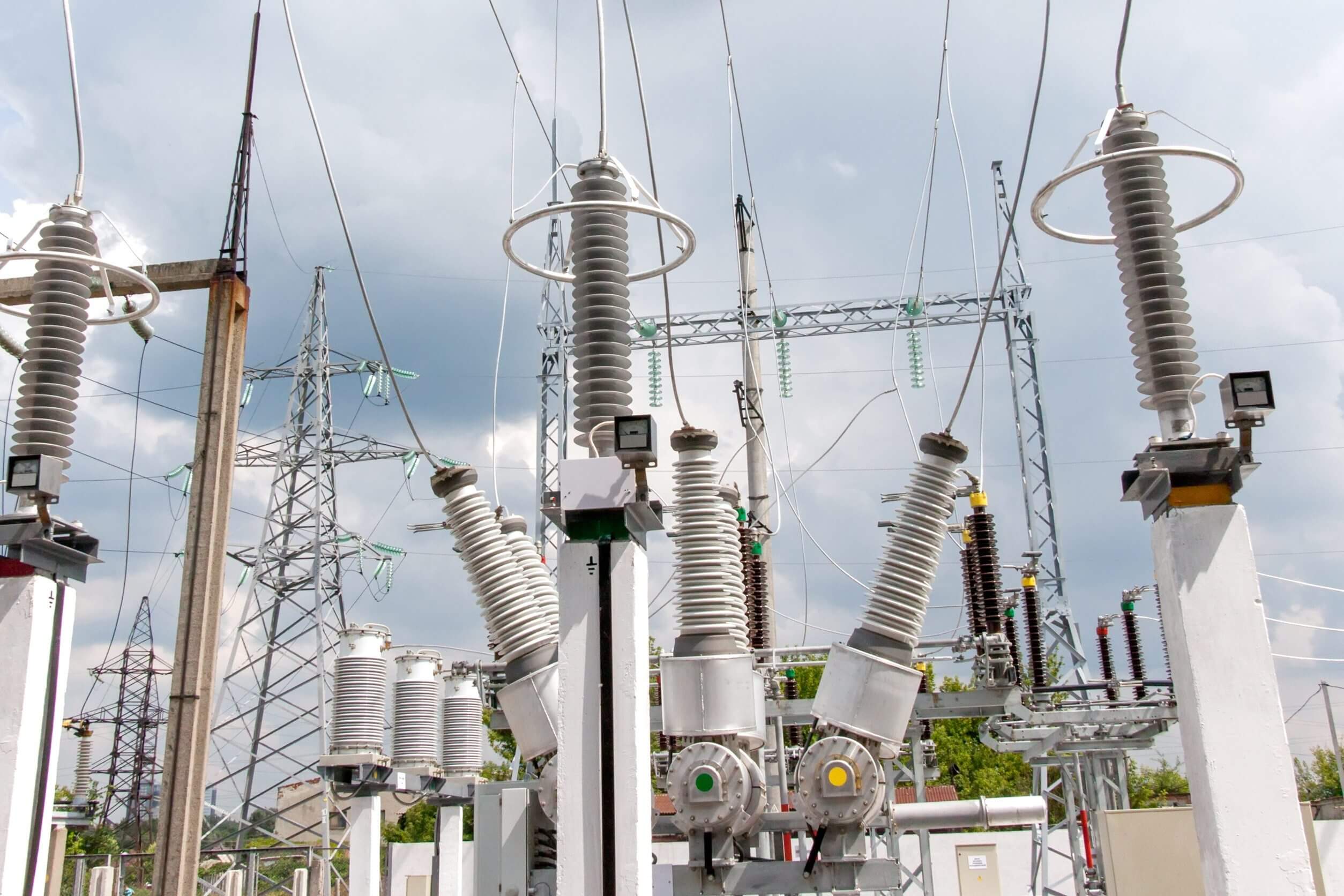 High-voltage equipment in an electrical substation under a cloudy sky.